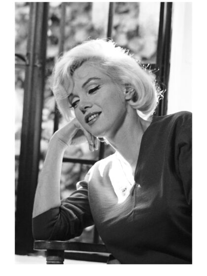 Schwarz-Weiß-Porträt von Marilyn Monroe mit geneigtem, auf die Hand gestütztem Kopf vor einem Fenste